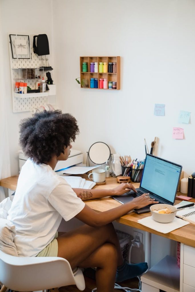 Woman concentrating while working on a laptop at a home office desk with creative supplies.